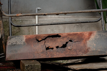 Close-up texture of a heavily corroded metal cylinder with large rust holes and orange oxidation.