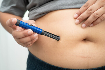 Asian woman injecting herself diabetes injecting insulin in stomach at home.
