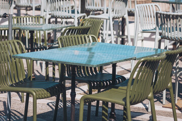 Outdoor seating area with green tables and chairs in a busy location during daylight hours filled with people walking by