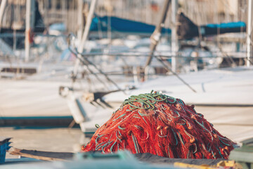 Bright red fishing net sits on dock as boats rest in harbor during late afternoon sunlight