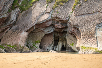 Seaside Cave Entrance Carved Into Colorful Rock Formations By Ocean Tide At Beach