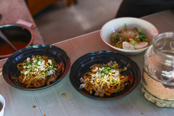 Delicious Asian noodle dish in black bowl on restaurant counter. savory lunch meal with fresh ingredients, meat, and tasty sauce creating an appetizing, authentic culinary experience