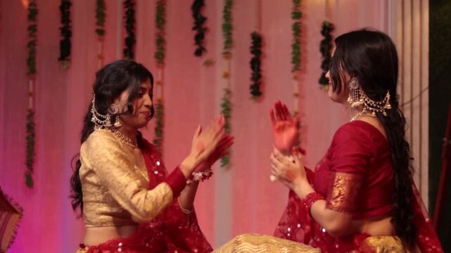 Indian girls playing traditional hand-clapping game while sitting indoors in festive attire