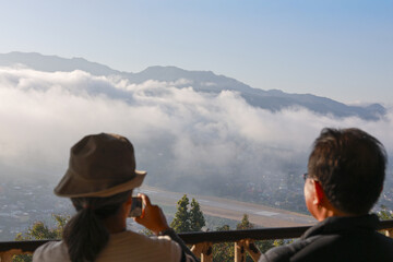 Peaceful asian couple on balcony enjoying scenic mountain view above cloud. woman in hat and man together look at beautiful landscape with sense of awe and wonder