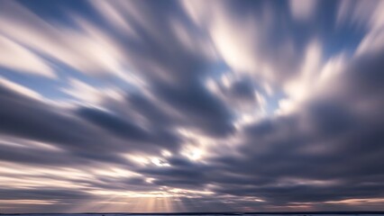 Dramatic long exposure of streaking clouds at sunset or sunrise with sun rays breaking through, capturing motion and atmosphere