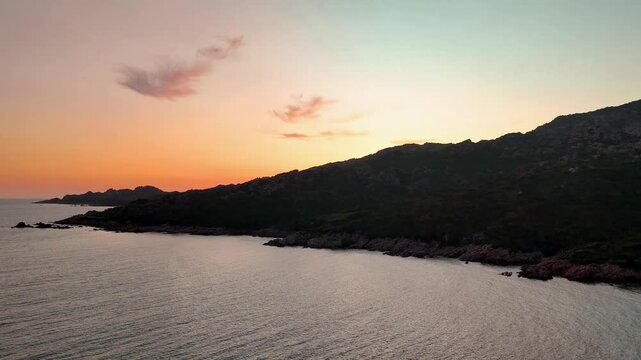 Cinematic aerial rise shot soaring over the rugged cape of Capu di Fenu, revealing the expansive Mediterranean Sea horizon and the dramatic golden hour sunset near Bonifacio, Corsica, France.