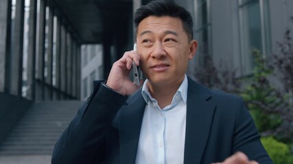 Smiling friendly talking phone Asian business man Chinese male Japanese investor trader real estate agent talk smartphone Korean businessman speaking in downtown satisfied joyful discussing in city