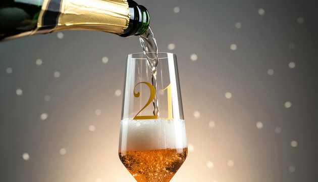 Glass engraved with the number 21. Champagne bottle fills the glass with alcohol. Celebrating milestone, anniversary or birthday