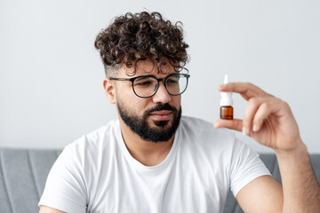 Man feeling skeptical, holding nasal spray for allergy or cold treatment