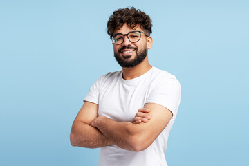 Young man smiling, wearing glasses and white t shirt, arms crossed, feeling confident