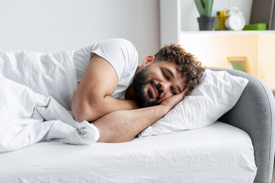 Young man sleeping peacefully in bed, achieving deep relaxation and pleasant dreams