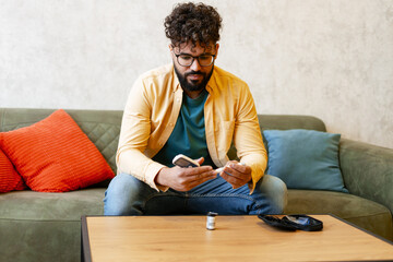 Young man using a glucometer at home, actively managing his health and diabetes