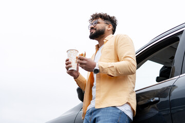 Young man enjoying a fast food meal and drink during a road trip break