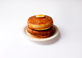 Pancakes with a pat of butter and syrup. Two thick pancakes are placed on a round plate.