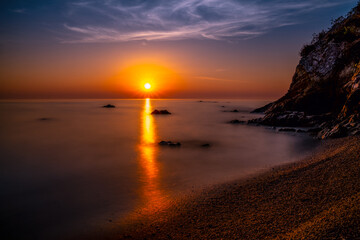 Romantischer Strand in der Dämmerung am Fusse eines Felsens