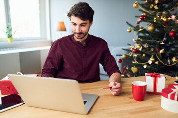 Picture of young man doing Christmas shopping using laptop paying with credit card