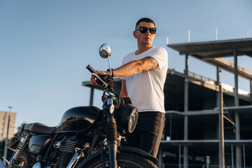 Construction site behind, posing. Man is outdoors with his motorcycle
