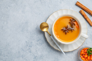 Sea buckthorn herbal tea in a cup on a light background with spices, berries and spoon.