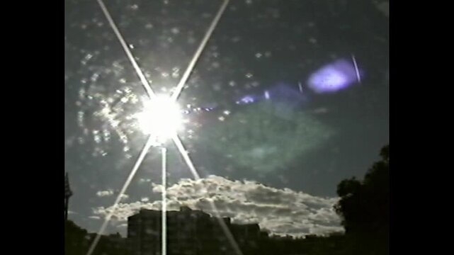 Retro-style sun glare with purple flare shapes seen above city rooftops and cloudy sky