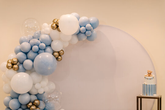 Trendy photo wall or zone decoration white, blue, gold balloons in hall restaurant. Delicious reception at birthday party. Celebration baptism concept. Cake on background decor for baby boy.