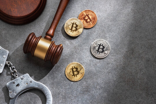 Judge gavel, handcuffs and Bitcoin coins on gray stone surface. Represents cryptocurrency regulation and crime.