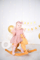 a little blue-eyed girl rides a wooden horse and celebrates her first birthday
