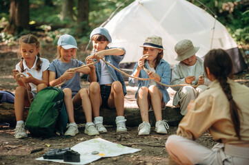 Survival tips, sitting at camp. Woman is doing tour for group of kids in the forest