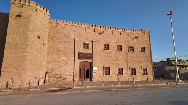 Ancient Mirbat stone fort with defensive towers and a flag flying high, standing in Mirbat city at dusk, highlighting historic Omani architecture and cultural heritage in Dhofar, in Oman at sunset
