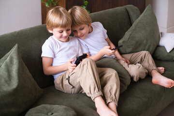 kids blonde boys twins using smartphones on the couch in living room