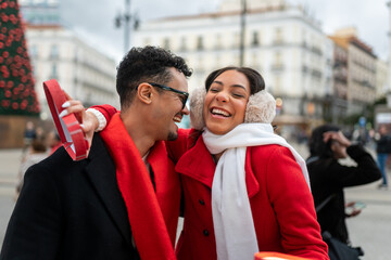 Excited couple sharing a gift, laughing and embracing outdoors in madrid during winter, celebrating christmas joy together