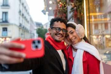 Young couple smiling, taking selfie with smartphone in madrid city during christmas holidays