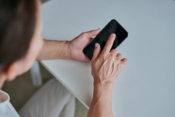 部屋でスマホを操作するシニア女性