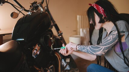 Woman repairing motorcycle in garage while wearing bandana and demonstrating mechanical skill with tools