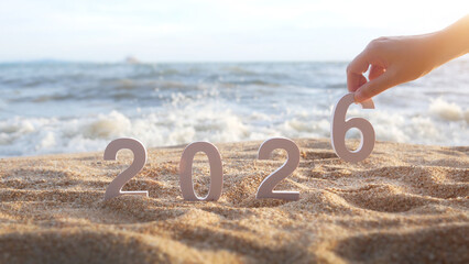 hand place the number 6 on sandy beach, transition from year 2025 to 2026 for new year sign on summer beach at sunset time, with ripple sea wave and beautiful nature at background, New Year celebrate