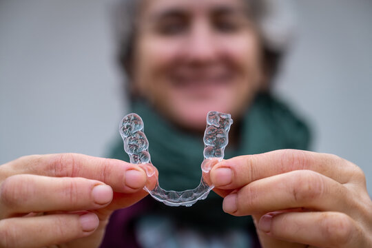 Senior woman smiling while holding an aligner for orthodontic treatment. Invisible clear plastic aligner improving dental health