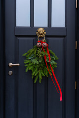 Close-up of a beautiful Christmas wreath with red ribbon and bells on a black door
