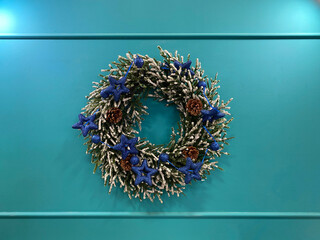 Christmas wreath with blue glitter stars and pinecones hanging on a teal wall.