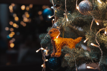 Obraz premium Cozy Christmas tree ornament with a handmade plush dog, glowing fairy lights and warm festive bokeh. Perfect for New Year 2026 ambience, holiday decor concepts, seasonal celebration design projects.