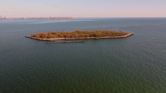 Aerial drone view of Hoffman Island in New York Harbor, a small historic island surrounded by calm open water with the distant coastline visible on the horizon.