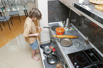 A young boy searching for cookware in an open kitchen drawer. Child helping at home