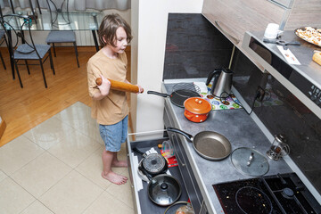 Young boy with a rolling pin in the kitchen. Child helping with cooking chores at home