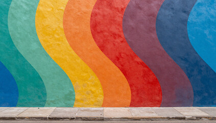 Vibrant rainbow painted on a wall next to a sidewalk.