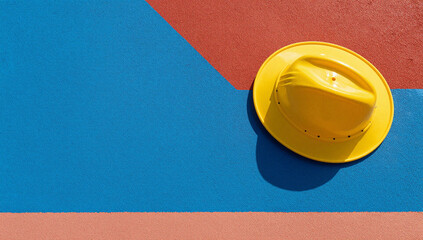 Yellow hard hat rests on a blue and red surface.