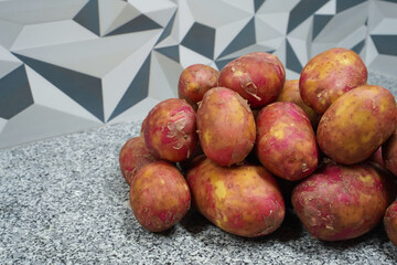 Red potatoes of the Asterix variety. Several washed potatoes with young skin are neatly stacked and isolated on a gray background of a kitchen. New potato harvest. Horizontal image, professional photo