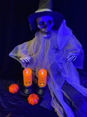 halloween witch with pumpkin. Halloween decoration with two orange LED candles in black holders, small pumpkins, and plastic spiders on a dark background with blue lighting and cobwebs
