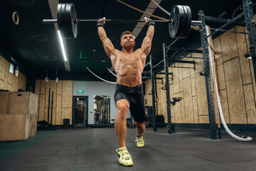 Workout session. Athletic man performing weightlifting exercises with a barbell in a gym