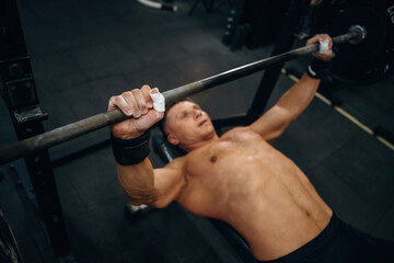 Lying down and pushing the barbell. Athletic man performing weightlifting exercises in a gym