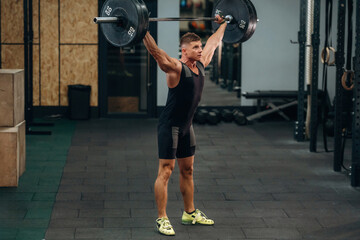 Side view. Athletic man performing weightlifting exercises with a barbell in a gym