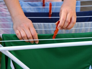 Woman hands using a clothespin to hang up laundry to dry on a drying rack. Close-up