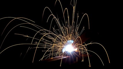 Brilliant golden welding sparks fly dramatically against absolute black background creating dynamic abstract light trails
